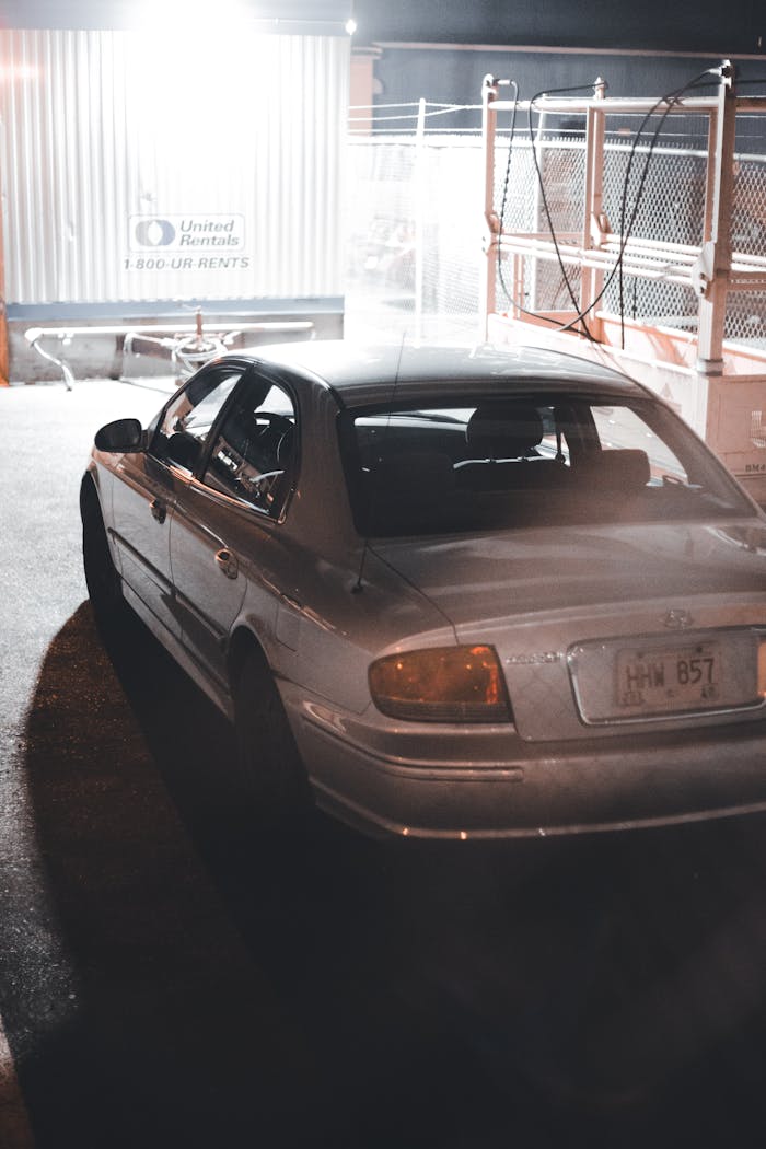 A sedan car parked at night under street lighting near an industrial site.