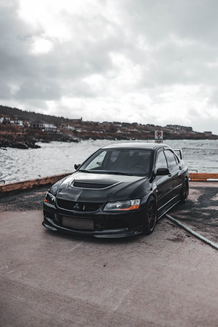 Home Black car parked on a waterfront, capturing a blend of modern automotive design and natural beauty.